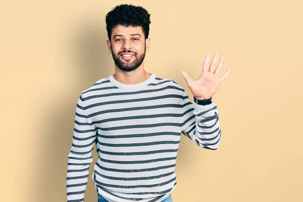 年轻的阿拉伯男子 留着胡子 穿着随意的条纹毛衣 手指头指向五号 面带微笑 自信而快乐 — 图库照片