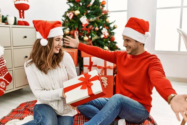Young Hispanic Couple Wearing Christmas Hat Opening Gift Home — Stock Photo, Image