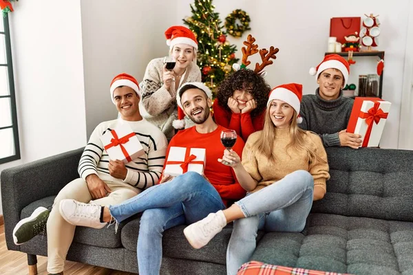 Gruppo Giovani Che Festeggiano Natale Bevendo Vino Tenendo Regali Seduti — Foto Stock