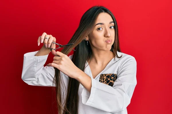 Young Hispanic Girl Cutting Hair Using Scissors Puffing Cheeks Funny — Stock Photo, Image