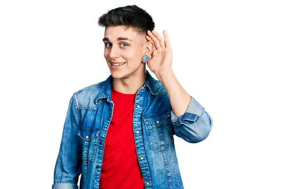 噂やゴシップに耳を傾け耳の上に手で笑みを浮かべてカジュアルなデニムジャケットを着て耳の拡張を持つ若い白人の少年 聴覚障害の概念 — ストック写真
