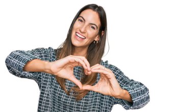 Genç ve güzel bir kadın, gündelik kıyafetler giyip, aşıkken gülümsüyor ve elleriyle kalp sembolü yapıyor. romantik kavram. 