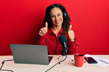 Güzel orta yaşlı bir kadın radyo stüdyosunda çalışıyor. Elleriyle olumlu jest yapıyor. Gülümsüyor ve başarı için mutlu. kazanan jest. 