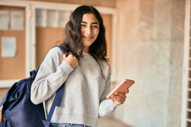 Genç ortadoğulu kız şehirde akıllı telefon kullanarak mutlu bir şekilde gülümsüyor..