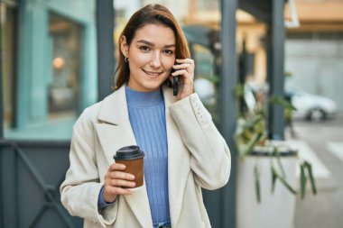 Genç İspanyol kadın akıllı telefondan konuşuyor ve şehirde kahve içiyor..