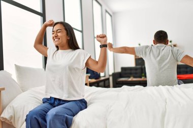 Genç latin çift, esniyor ve kollarını uzatıyor yatağa oturuyorlar..