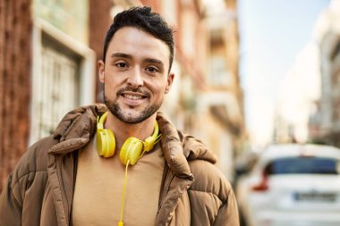 Şehirde kulaklık takarak mutlu gülümseyen genç İspanyol adam..