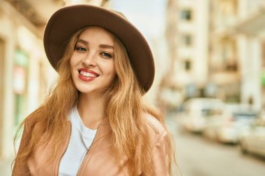 Genç sarışın kız gülümsüyor, mutlu bir şekilde şehirde duruyor..