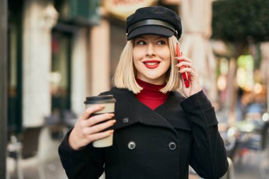 Genç sarışın kadın akıllı telefondan konuşuyor ve şehirde kahve içiyor..