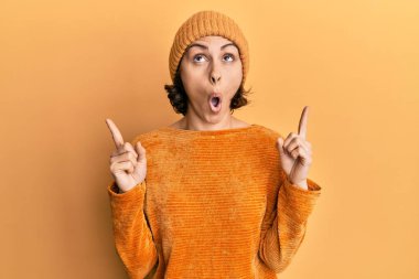 Genç esmer kadın yün şapka ve kışlık süveter giyiyordu. Şaşırmış ve şaşırmıştı. Parmaklarıyla işaret ediyor ve kollarını kaldırıyordu.. 