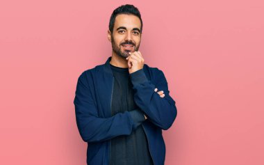 Gündelik kıyafetler giyen genç İspanyol adam kameraya bakıyor kollarını kavuşturup gülümseyerek ve çenesini kaldırarak. Olumlu düşünmek. 