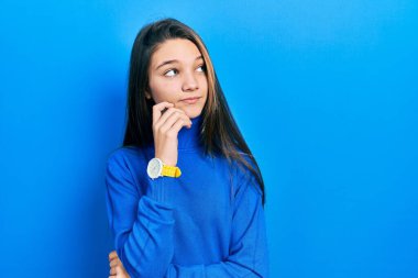 Balıkçı yaka kazak giyen, eli çenesinde soru soran genç esmer kız, düşünceli bir ifade. Gülümseyen ve düşünceli bir yüz. şüphe kavramı. 