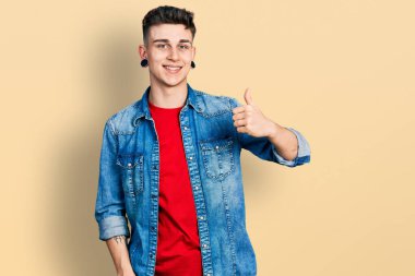 Kulakları genişlemiş, sıradan bir kot ceket giymiş, el hareketleriyle mutlu mesut hareket eden beyaz bir çocuk. Kameraya bakıp başarıyı gösteren ifade. 