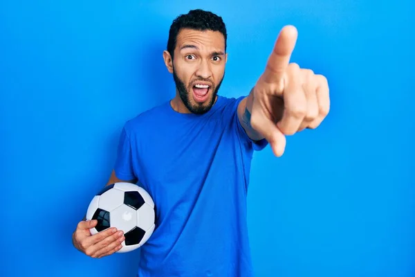 Hispanic Man Beard Holding Soccer Ball Pointing Finger Surprised Ahead — Stock Photo, Image