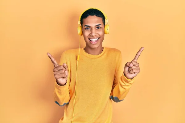 年轻的非洲裔美国人 一边用耳机听音乐 一边用手指指向不同方向 自信地微笑着 复制广告空间 — 图库照片