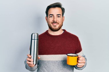 Sakallı, kahve içen, yüzünde mutlu ve serin bir gülümsemeyle gülümseyen yakışıklı beyaz adam. diş gösterme. 