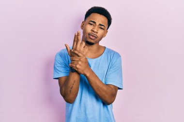 Sıradan mavi tişört giyen genç Afro-Amerikan bir adam sembolik bir silah taşıyor, el hareketleriyle cinayet silahlarıyla oynuyor, kızgın bir surat takınıyor. 