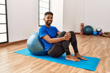 Yakışıklı İspanyol adam egzersiz yapıyor ve yoga minderinde geriniyor, spor salonunda pilates topuyla esneklik gösteriyor.