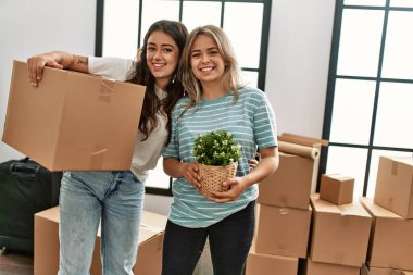 Mutlu bir şekilde gülümseyen genç bir çift yeni evine karton kutu ve saksı yerleştiriyor..