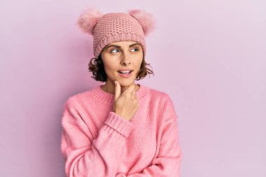 Genç esmer kadın, elleri çenesinde sevimli yün şapkalı soru soran, düşünceli bir ifade takınıyor. Düşünceli bir yüzle gülümsüyor. şüphe kavramı. 