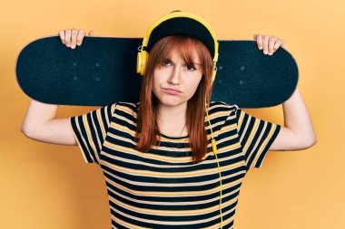 Kulaklık takan kızıl saçlı genç bir kadın şüpheci ve gergin, sorun yüzünden suratını asıyor. negatif kişi. 