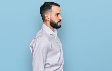 Sakallı genç bir adam iş gömleği giyiyor. Taraf arıyor, rahat poz veriyor. Kendine güvenen bir gülümsemesi var.. 