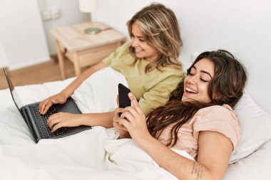 Genç çift akıllı telefon kullanıyor ve yatak odasında film izliyor.