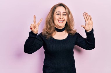 Orta yaşlı, beyaz, günlük kıyafetler giyen, 7 numaralı parmaklarıyla işaret eden, kendinden emin ve mutlu bir kadın.. 