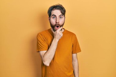 Sakallı, sıradan sarı tişörtlü beyaz bir adam. İnançsızlığa, şaşkınlığa ve elleri çenesinde şaşkınlığa kapılmış bir ifade. 