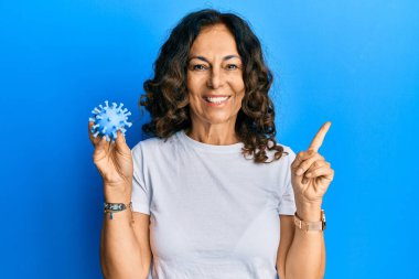 Orta yaşlı İspanyol kadın elinde virüs oyuncağı tutarken gülümsüyor. 