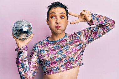 Makyaj yapan yakışıklı bir adam elinde parlak disko topuyla komik suratlı yanakları şişiriyor. Ağzı havayla şişer, havayı yakalar.. 