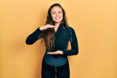 Genç İspanyol kız dalgıç neoprene üniforması giyiyordu. Elleri büyük ve büyük bir işaret gösteriyordu. Ölçü sembolü. Kameraya bakıp gülümsüyor. ölçüm kavramı. 