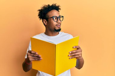 Sakallı, kitap okuyan, gözlüklü, gülümseyen ve kafasını çeviren genç Afrikalı Amerikalı bir adam.. 