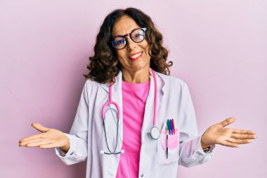 Orta yaşlı İspanyol kadın doktor üniforması giyiyor ve gözlük takıyor. Kolları ve elleri havada, kafası karışmış bir ifade takınıyor. şüphe kavramı. 