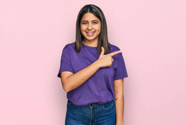Genç İspanyol kız, günlük mor tişört giyiyor. Neşeli. Yüzünde mutlu ve doğal bir ifadeyle elleri ve parmaklarıyla yüzünü gösteren bir gülümseme var. 