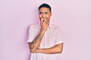 Gündelik kıyafetler giyen genç Afro-Amerikan adam gergin görünüyor ve elleri ağzında tırnak yiyor. anksiyete. 