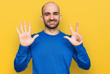 Gündelik kıyafetler giyen genç İspanyol adam sekiz numarayı gösterip işaret ederken kendinden emin ve mutlu bir şekilde gülümsüyor.. 