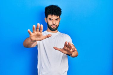 Sakallı, beyaz tişörtlü genç bir Arap. Avuç içi hareketlerini, sinirli ve hayal kırıklığına uğramış ifadesini durduruyor. 