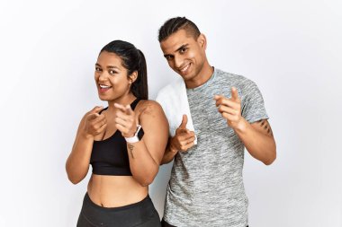 Spor kıyafetleri giymiş genç bir çift izole arka planda durup mutlu ve komik yüzlü parmaklarını kameraya doğrultuyor. iyi enerji ve titreşimler. 