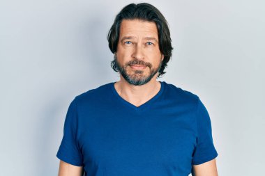 Yüzünde ciddi bir ifade olan günlük kıyafetler giyen orta yaşlı beyaz bir adam. Basit ve doğal bir şekilde kameraya bakıyorsun.. 