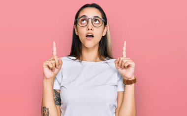 Gündelik beyaz tişört giyen genç İspanyol kadın şaşkın şaşkın yukarı bakıyor ve parmaklarıyla işaret ediyor ve kollarını kaldırıyordu.. 