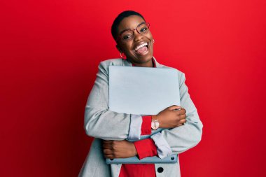 Genç Afrikalı Amerikalı iş kadını dizüstü bilgisayarını tutuyor ve kameraya seksi bir ifadeyle bakıyor, neşeli ve mutlu bir yüzle.. 