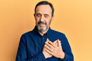 Orta yaşlı İspanyol bir adam, sıradan kıyafetler giyiyor, elleri göğsünde gülümsüyor, gözleri kapalı, yüzünde minnet ifadesi var. sağlık kavramı. 