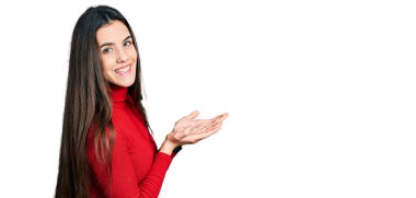 Kırmızı balıkçı yaka kazak giyen genç esmer kız avuçlarını açıp fotokopi alanını gösteriyor. 