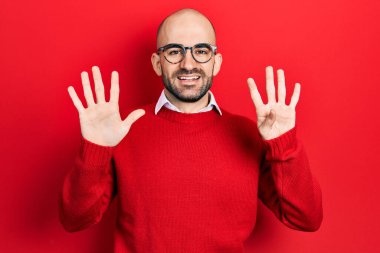 Genç kel adam, günlük kıyafetler ve gözlük takıyor. Dokuz numaralı parmaklarıyla gösteriyor ve işaret ediyor. Kendinden emin ve mutlu gülümsüyor.. 