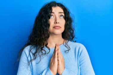 Kıvırcık saçlı genç esmer kadın. Günlük kıyafetler giyiyor. Elleriyle yalvarıyor ve dua ediyor. Yalvarıyor. 