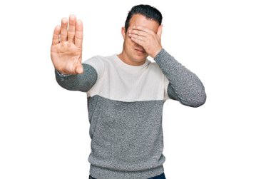 Kış süveteri giyen yakışıklı genç adam elleriyle gözlerini kapatıyor ve üzgün ve korku ifadeleriyle jest yapıyor. utangaç ve olumsuz kavram. 