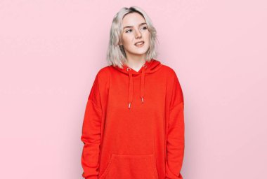 Sıradan kıyafetler giyen genç sarışın kız yüzünde gülümsemeyle yan yana bakıyor, doğal bir ifade. Kendinden emin gülen. 