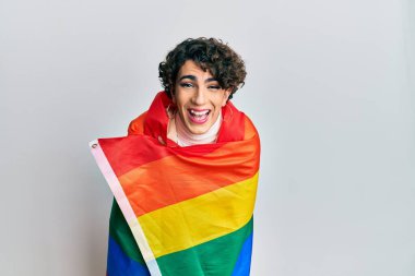 Gökkuşağı lgbtq bayrağına sarılı kadın makyajı yapan genç adam kahkahalarla gülüyor.. 