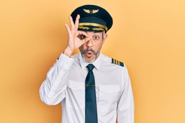 Gri saçlı, uçak pilotu üniforması giyen yakışıklı orta yaşlı bir adam şaşırmış yüz ifadesiyle şaşırmış, parmaklarından bakan bir jest yapıyor. İnançsız ifade. 